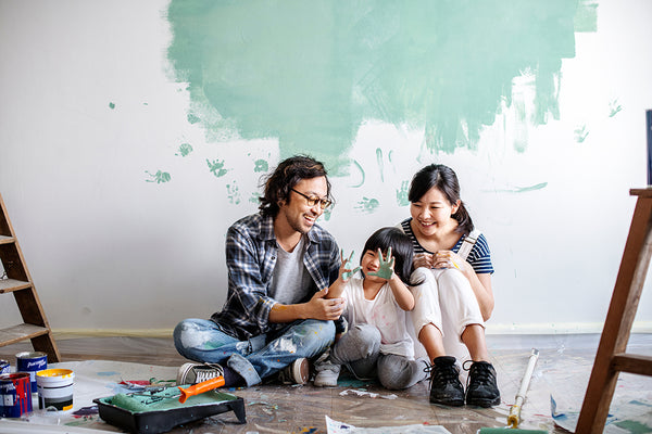 Young couple sits on the floor with child, taking a break from painting their wall with green paint.